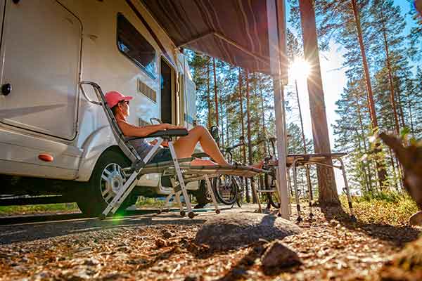 Mother sunbathing in lounge chair outside of rv camper with trees