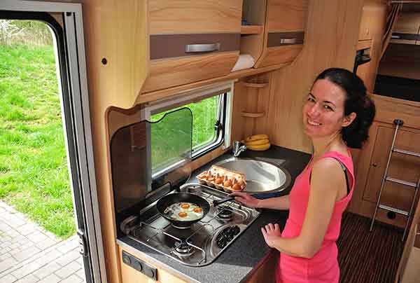 Smiling lady cooking bacon & eggs for breakfast on rv camper stove