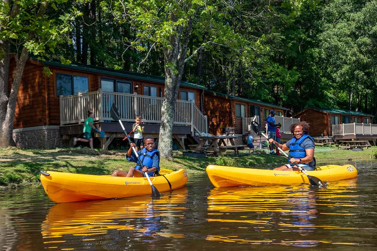 MOther and son paddling kayaks in front of lakeside camp cabins on cool springs lake at WIlderness Presidential resort in fredericksburg virginia