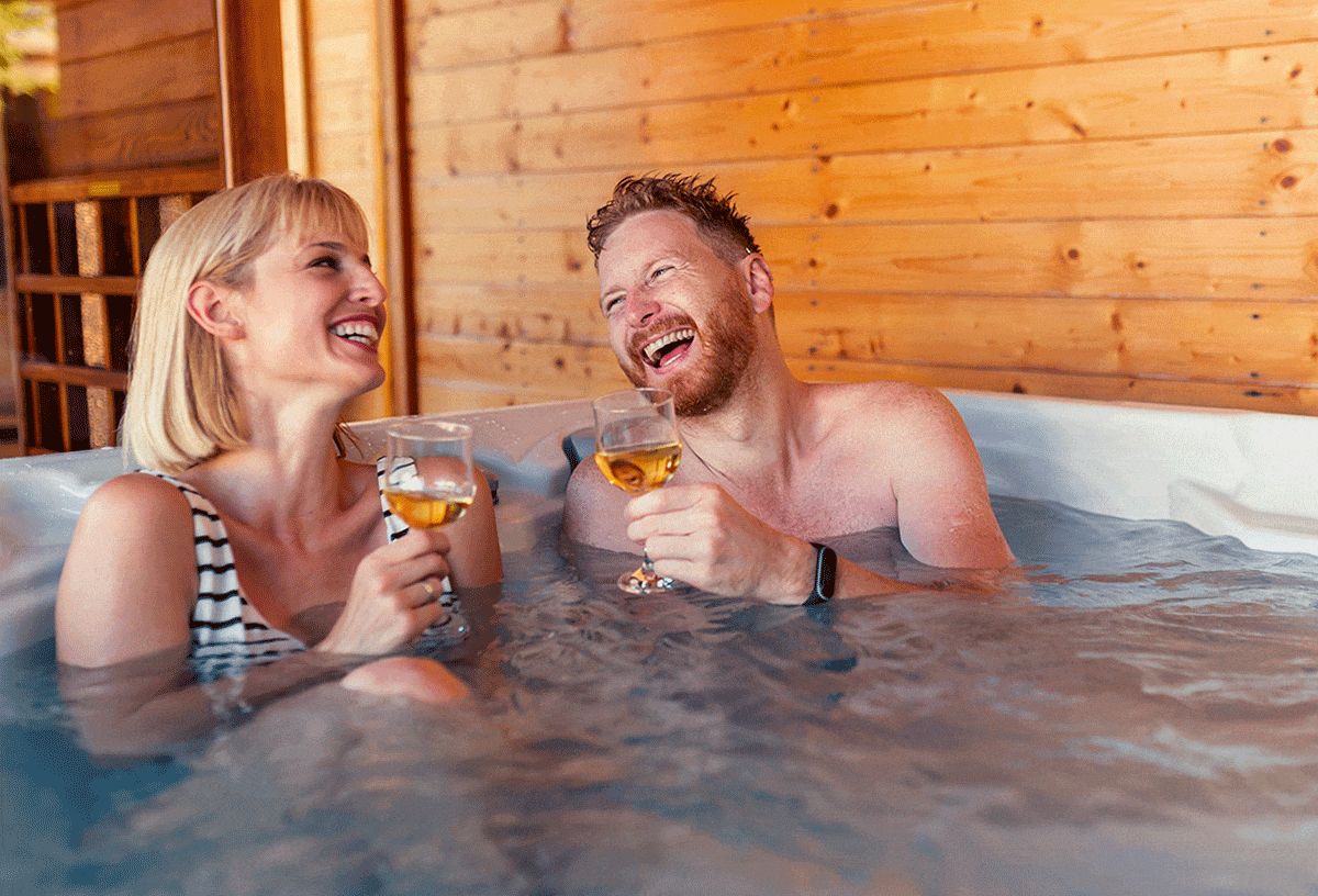 romantic couple sipping wine in a hot tub at a lakeside cabin